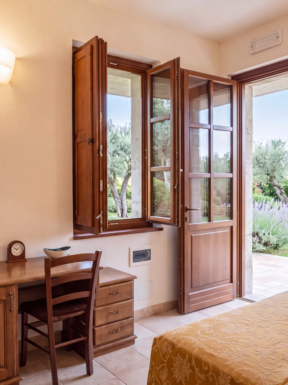 Una camera con la scrivania in legno e la porta-finestra aperta sugli ulivi
