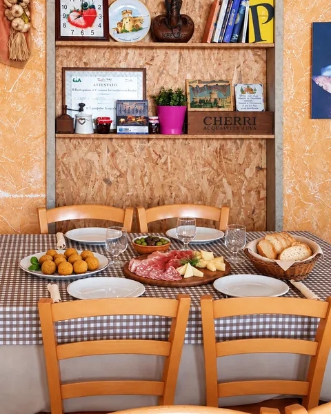 Una tavola della trattoria con la tovaglia a quadretti, olive all'ascolana, salumi e formaggi
