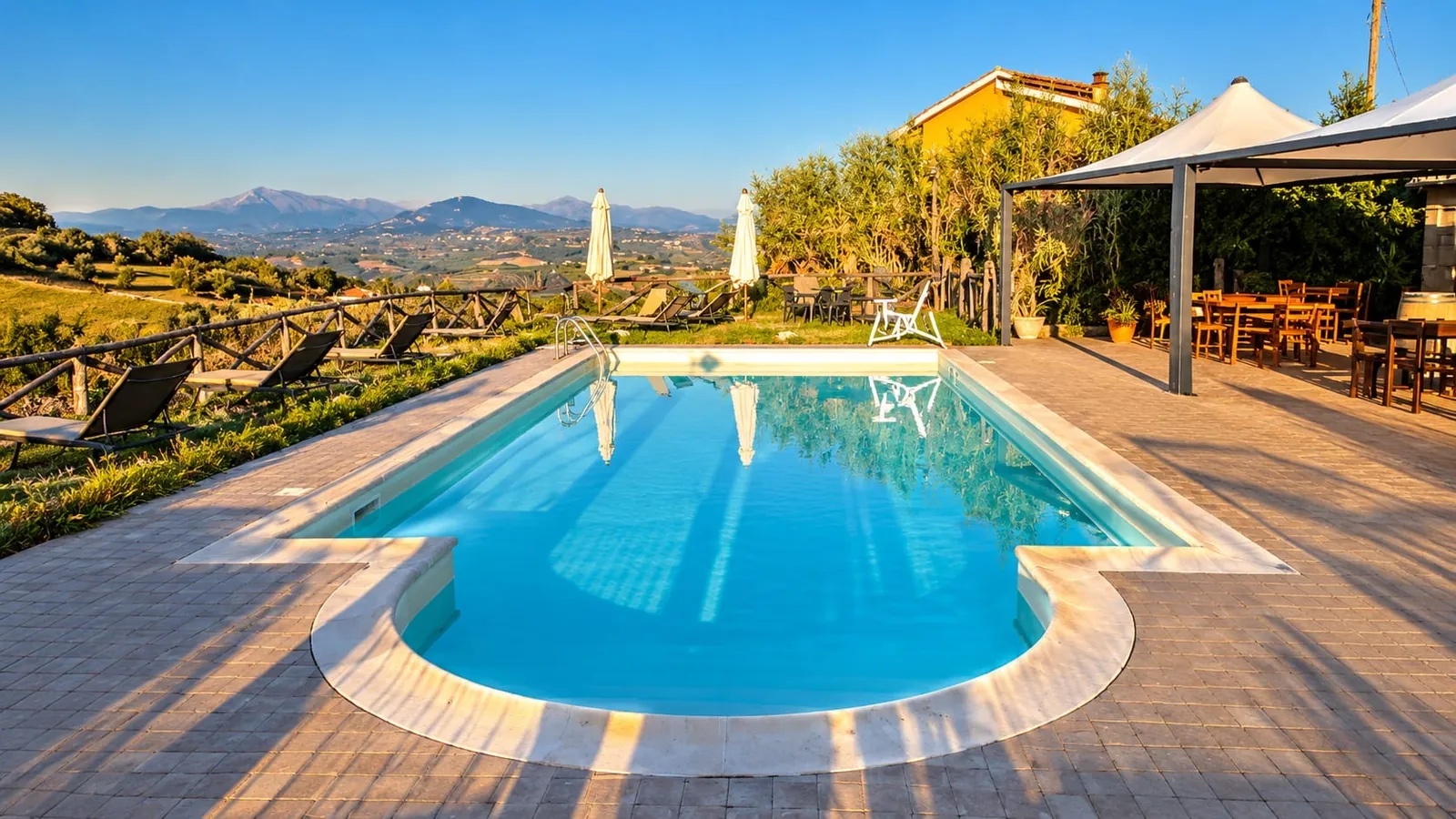La piscina con i lettini e il gazebo, con le colline e le montagne sullo sfondo