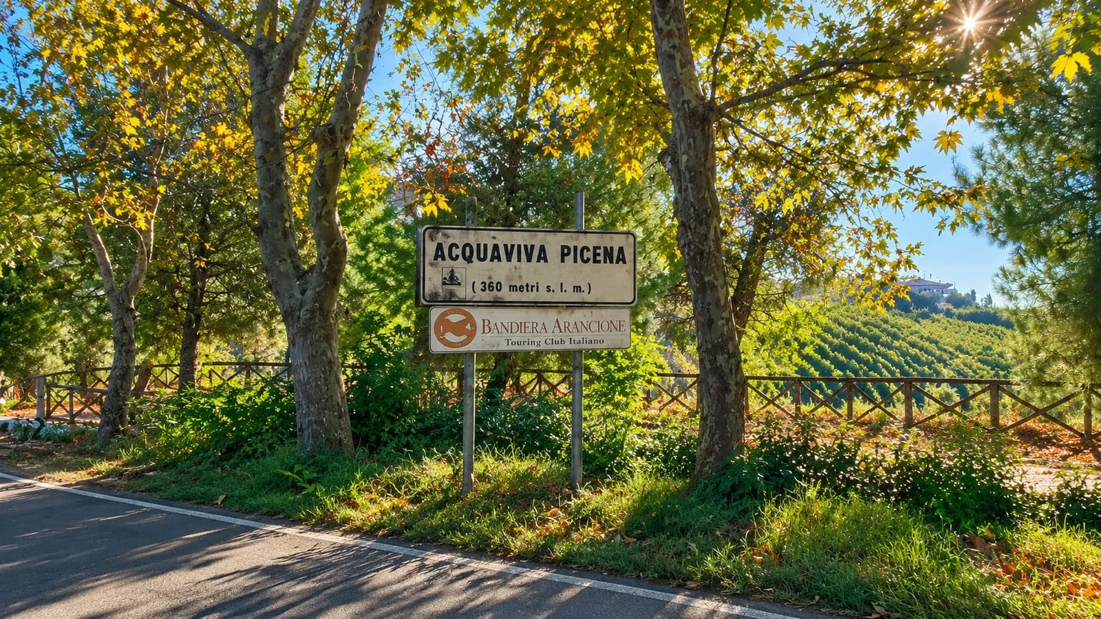 Il cartello di Acquaviva Picena con la Bandiera Arancione del Touring Club, lungo la strada tra gli alberi